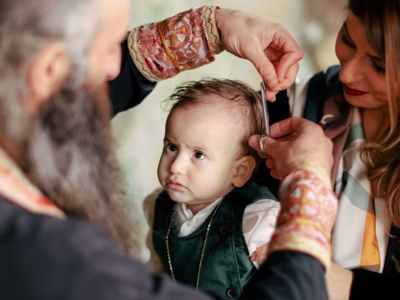 A baby's first haircut performed during a religious ritual with parents and clergy present.