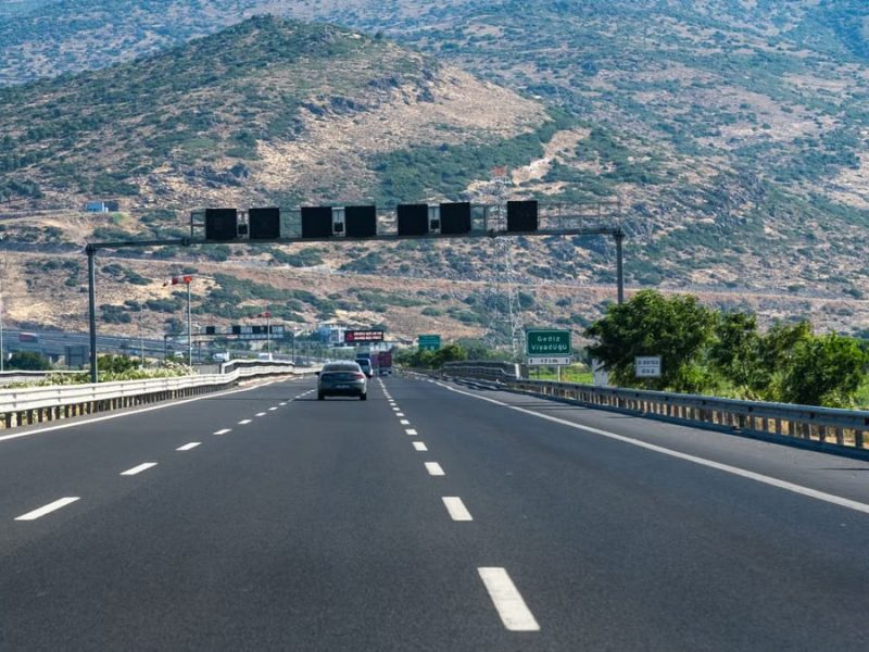 Long highway with cars traversing through rocky hills under blue skies, perfect travel scene.